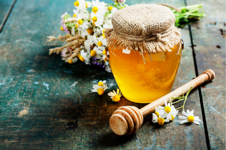 jar of precious raw and real honey aside a bouquet of daisies on a wooden table