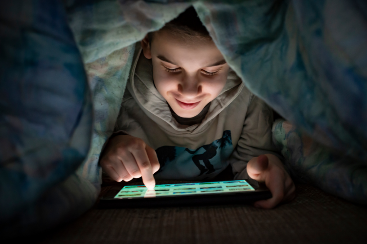 a teenager scrolling on a tablet in bed