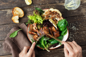 2 hands cutting vibrant and beautiful foods on a plate. Wooden table, linen napkin.