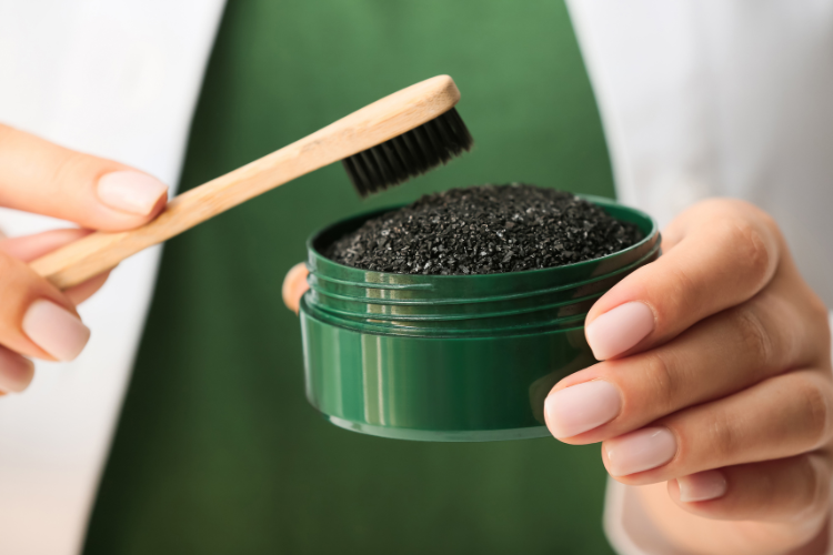 a person dipping a bamboo toothbrush into a pot of charcoal powder