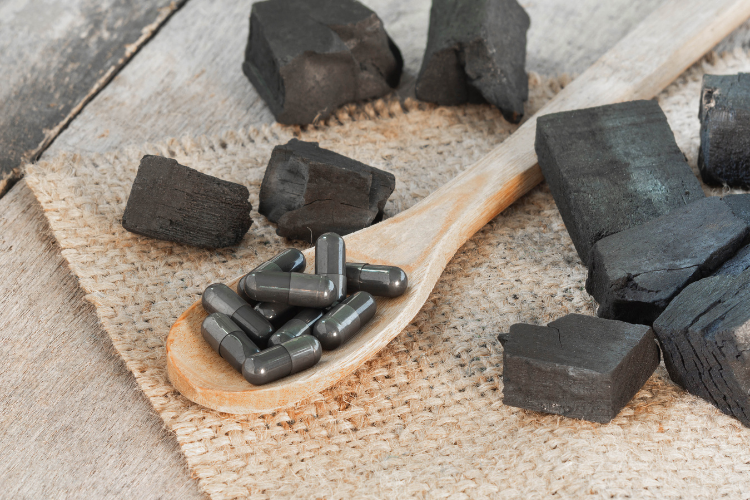 natural charcoal and charcoal capsules in a wooden spoon