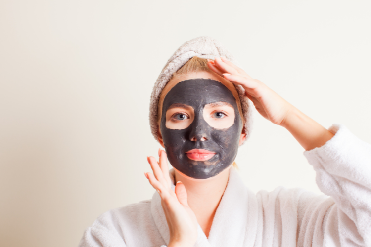 a woman wearing a charcoal mask on her face and a hair towel